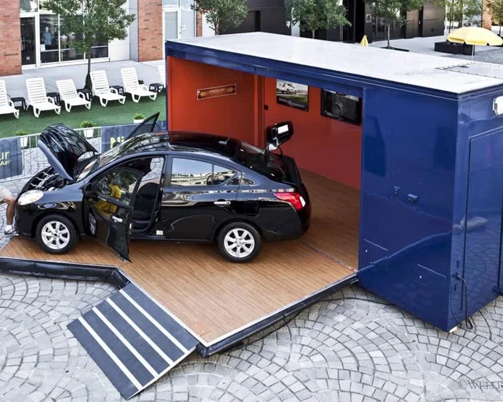 Nissan Leaf mobile showroom trailer with a black sedan displayed on a wooden deck and a loading ramp extended.