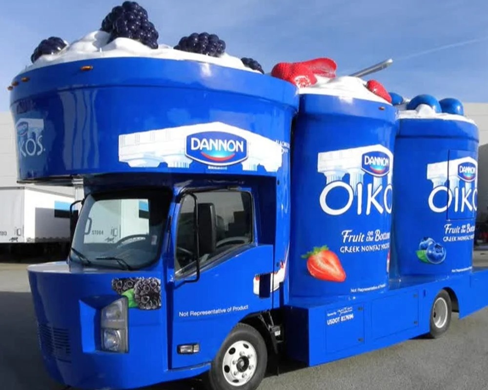 Dannon Oikos custom food truck built with giant blue yogurt containers and fruit props on top, created by custom food truck builders.