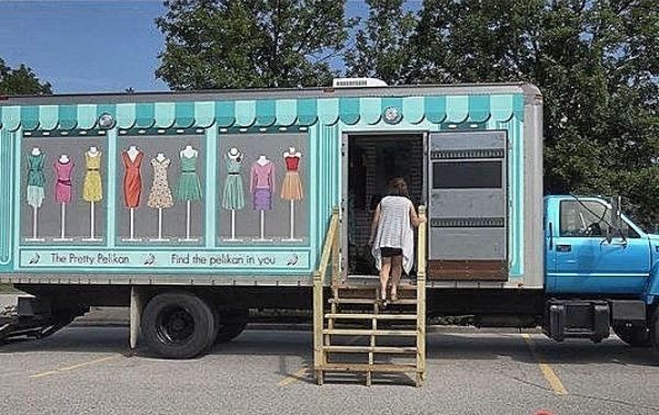 The Pretty Pelikan fashion truck, a mobile boutique with a teal striped awning design and clothing displays, as a woman steps up into the entrance.