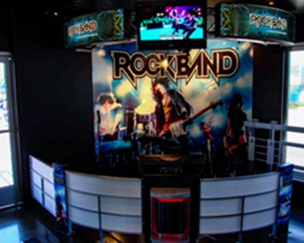 Dedicated Rock Band mobile gaming station with branded backdrop, screen, and curved counter.