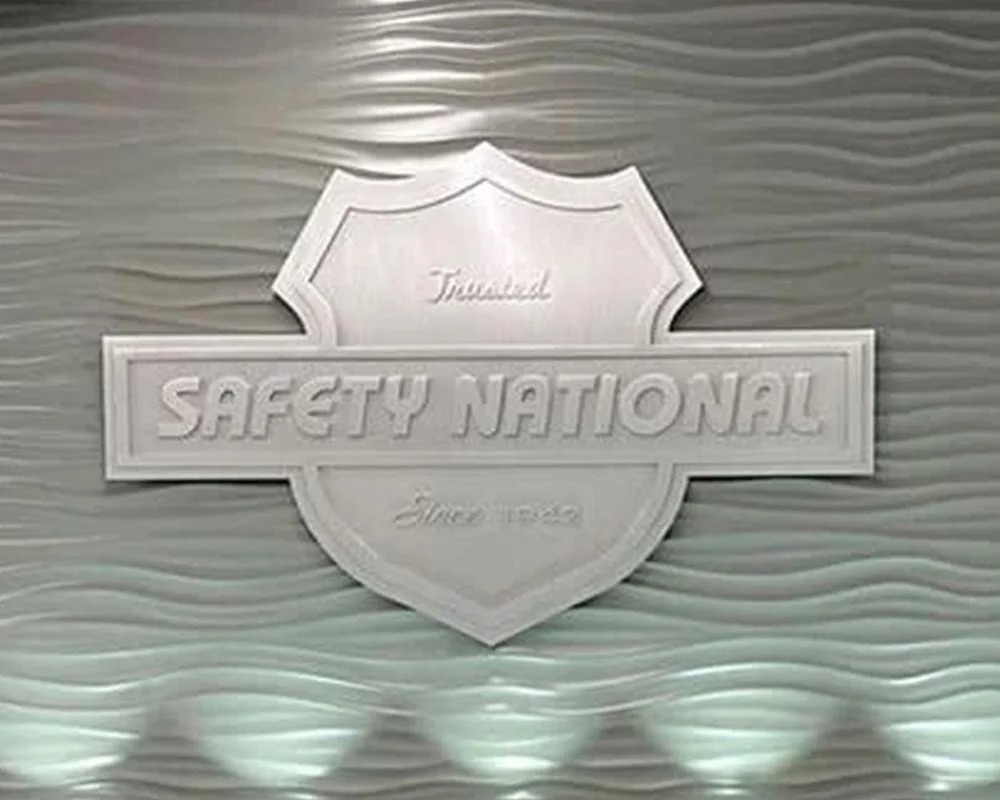 White dimensional Safety National shield logo and lettering sign mounted on a textured, backlit interior wall.1