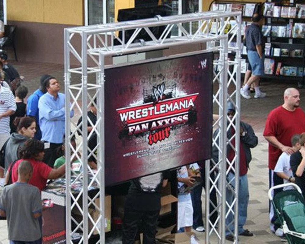 WrestleMania Fan Axxess Tour sign on a large screen mounted on metal trussing at an outdoor event.